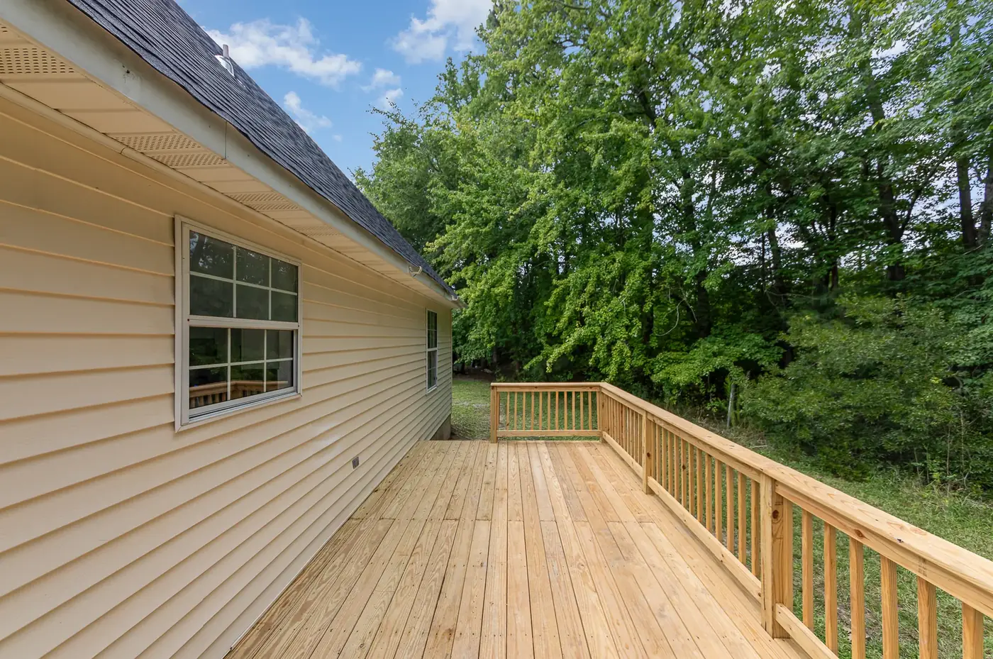 Home with new siding and a wide pressure-treated deck with railings alongside it