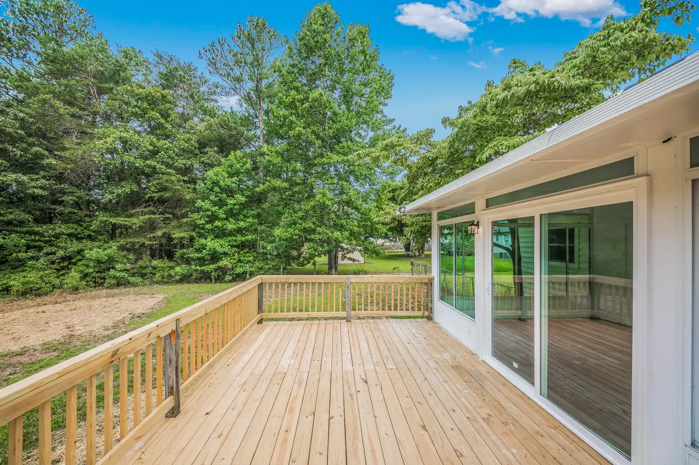 Wide timber rear deck with railings and sliding doors into the house
