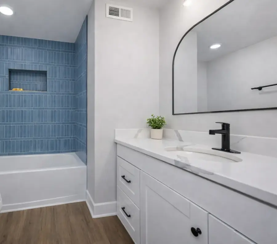 Bathroom with a blue-tiled tub surround, white vanity, black fixtures and an arched mirror