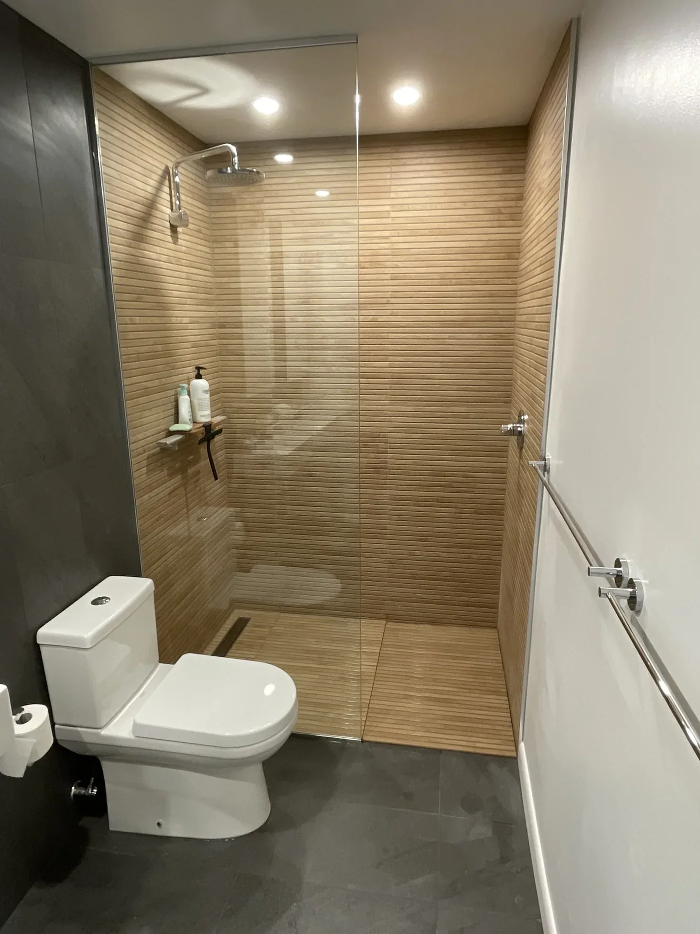 Bathroom with a wood-slat feature wall and glass shower screen, fixtures part-way through installation