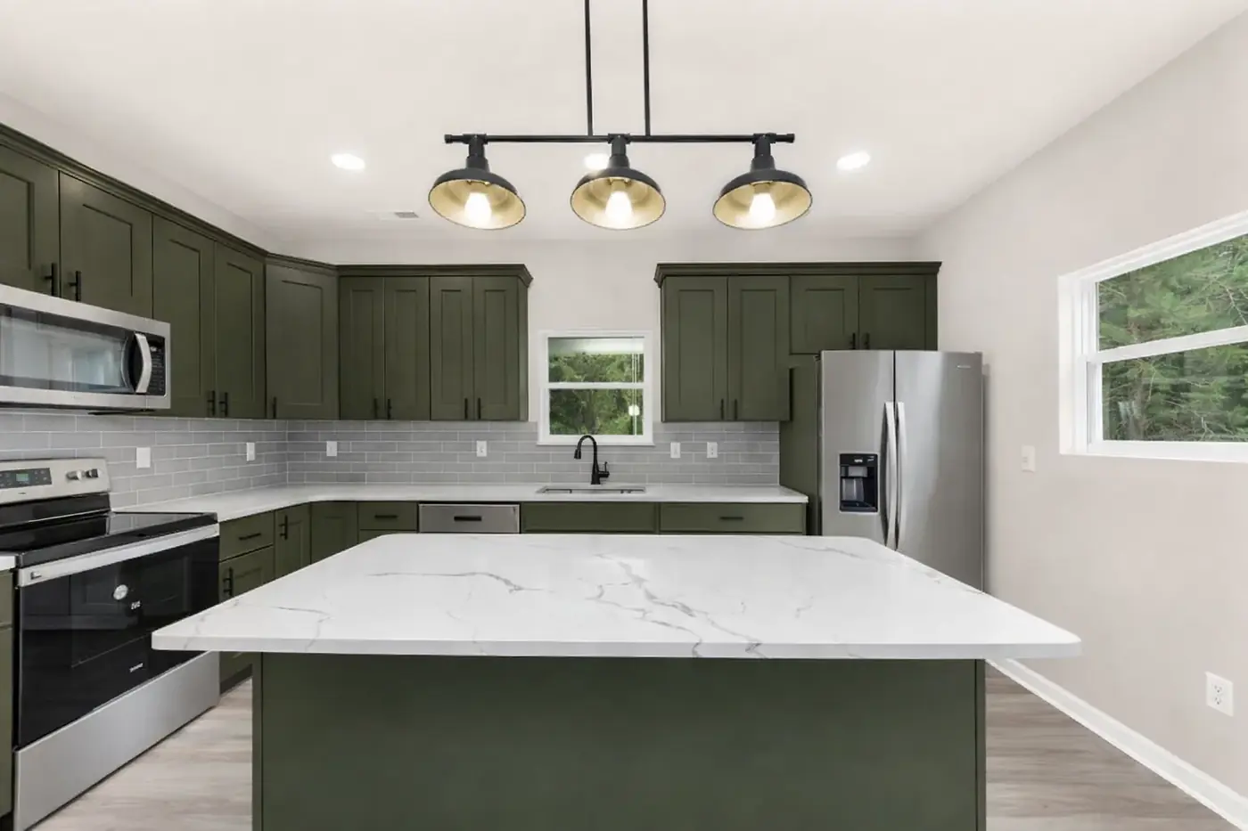 Green kitchen cabinetry with a white quartz island and glass pendant lights
