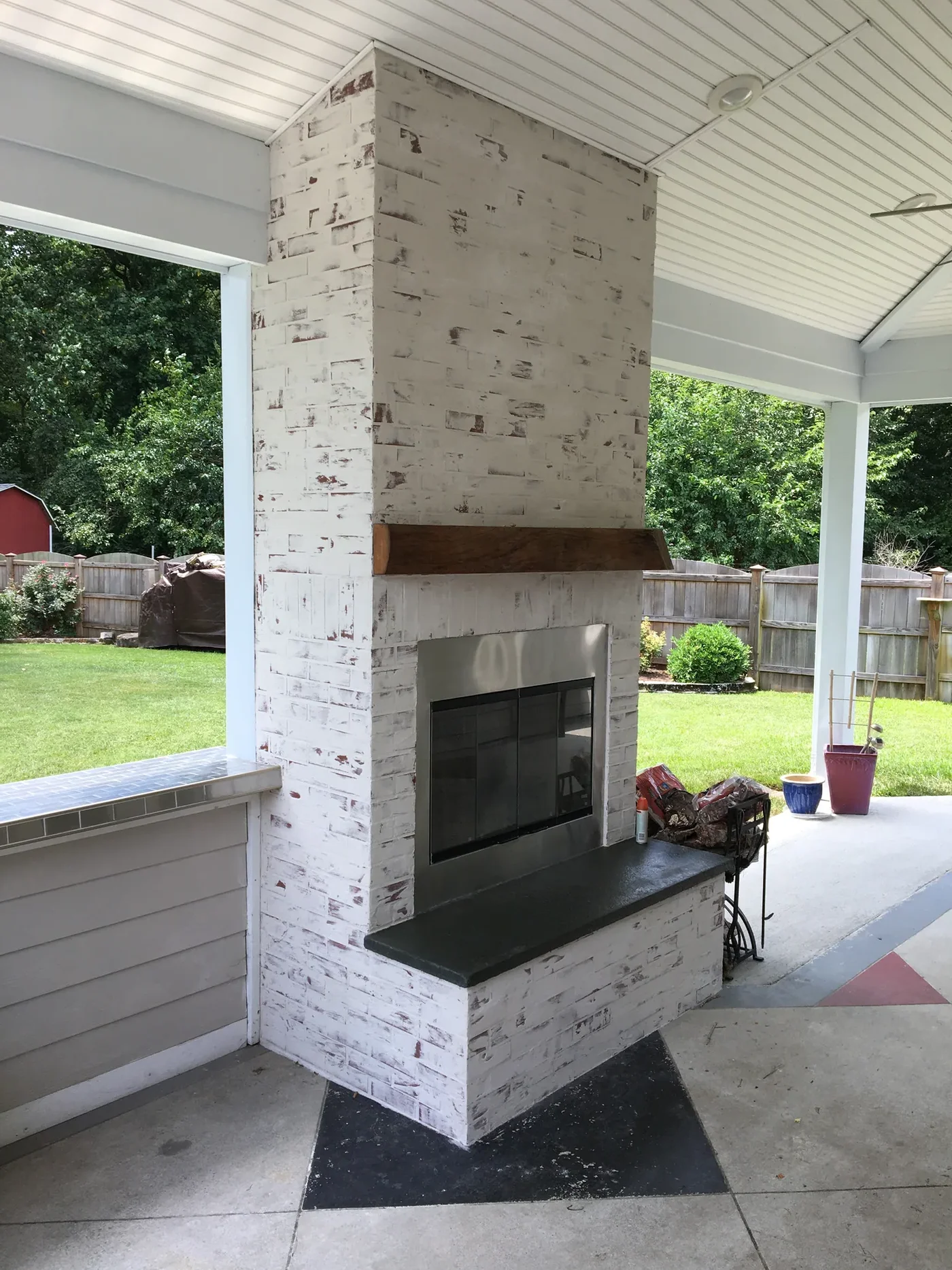 Outdoor stone-veneer fireplace with a wood mantel on a covered patio, seen from below